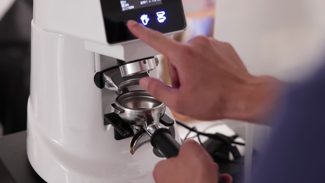 Barista profissional ou garçonete pressionando o botão na máquina moedora de café elétrica para moer grãos de café frescos em pó no porta-filtro para fazer uma bebida quente de espresso em uma cafeteria.