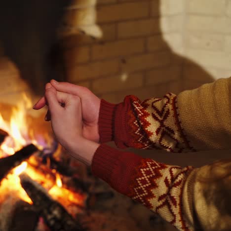 Hands of a man and woman near the fireplace. Couple in love warming hands by fireplace indoors. Romantic atmosphere at home.