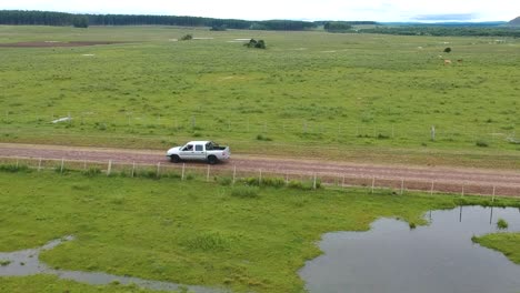 Toma-Aérea-Siguiendo-A-Un-Camión-Blanco-Conduciendo-A-Través-De-Pastizales-De-Uruguay