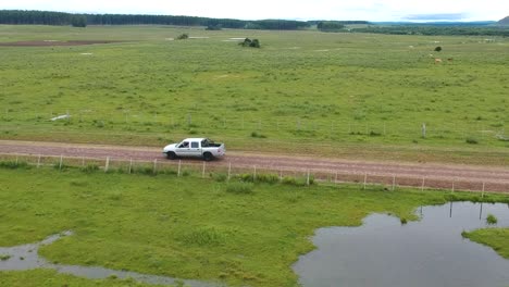 aerial shot following a white truck driving through grasslands of uruguay