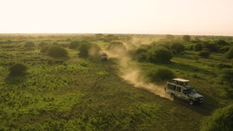 Autos,-Die-Durch-Trockene-Afrikanische-Ebenen-Fahren-Und-Bei-Sonnenuntergang-Staub-Aufwirbeln,-Von-Oben-Verfolgt