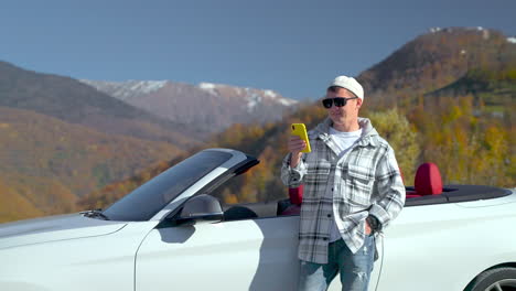 man taking a photo with his phone in a convertible car in the mountains.