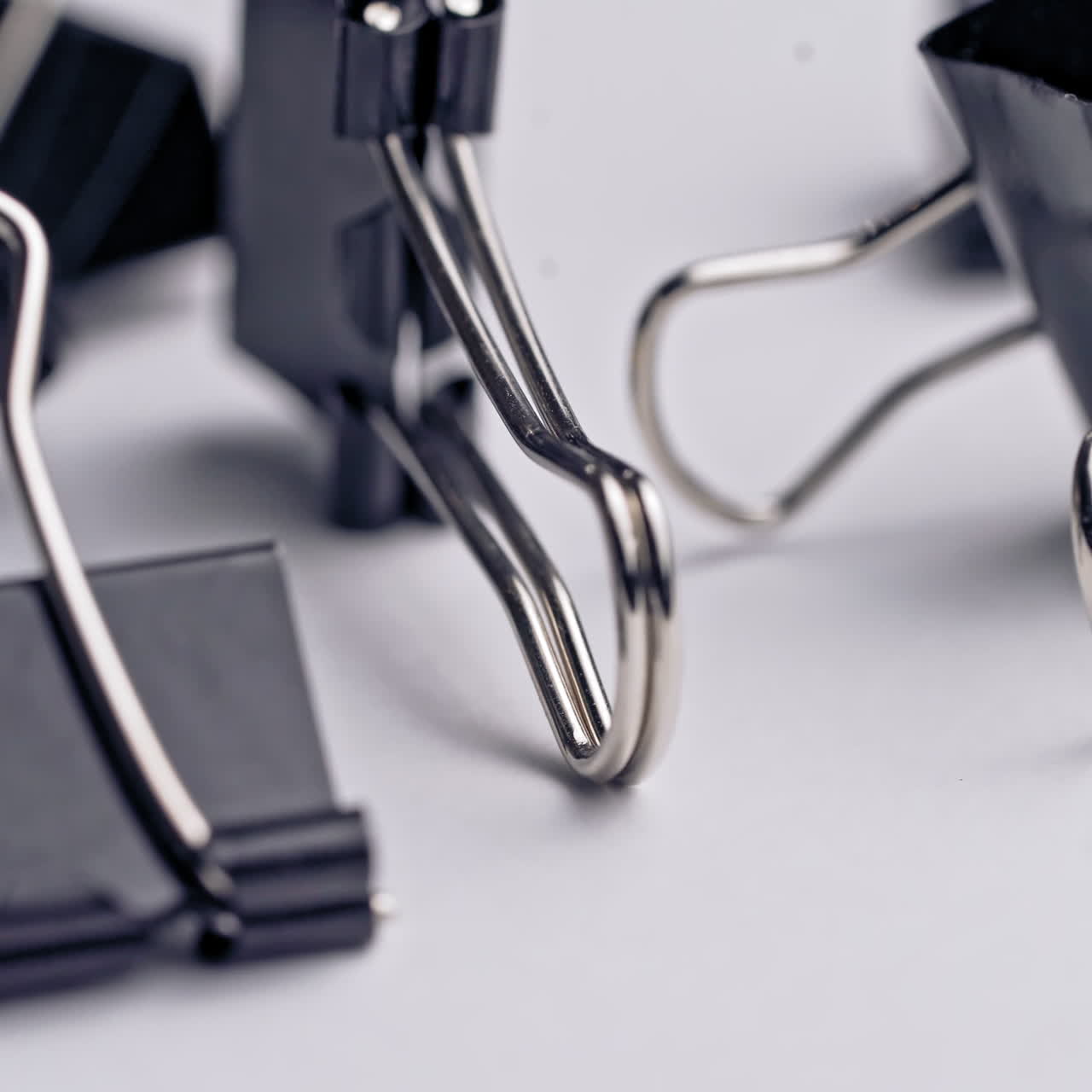 Black paper clips rotate on white background. Office supplies