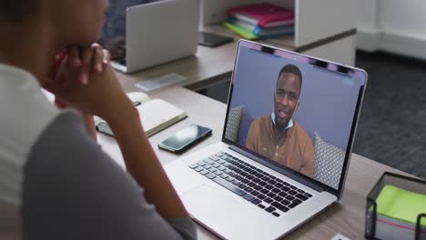 sección media de una mujer afroamericana haciendo una videollamada con un colega masculino en una computadora portátil en la oficina