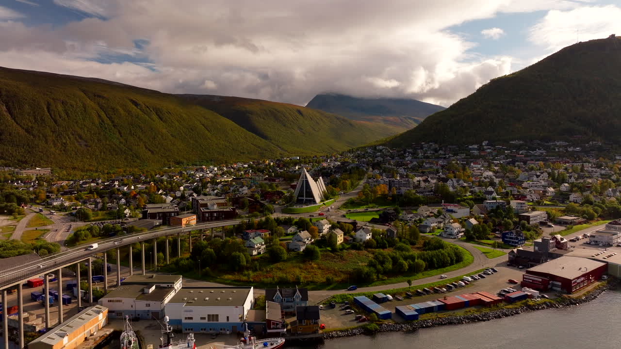 Sweeping drone reveal of the distinctive triangular Arctic Cathedral and surrounding Tromsø valley in fall, Norway – modern architecture meets dramatic Arctic landscape