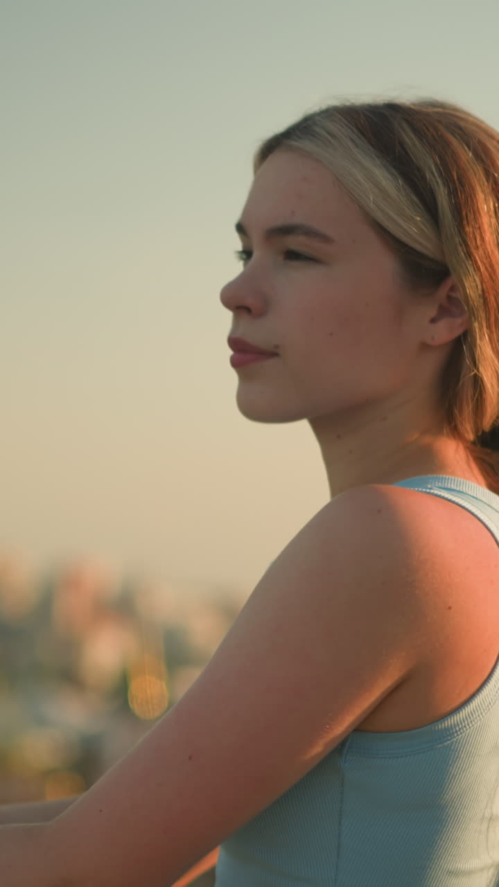 joven de pie al aire libre con las manos en la barandilla de hierro, mirando pensativo en la distancia bajo la cálida luz del sol, el paisaje urbano borroso en el fondo