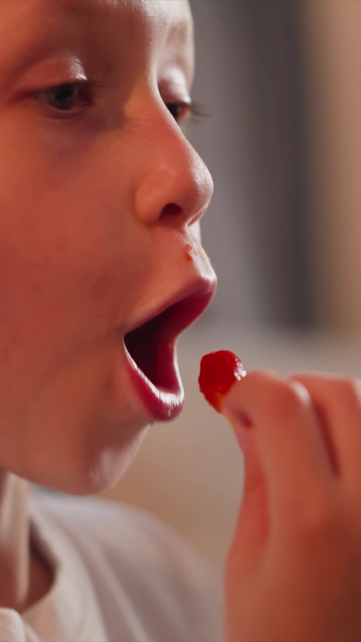 Close up of young girl eating food holding and bringing small pieces to her mouth. Her hand with painted nails is visible as girl interacts with edible item. Soft indoor lighting creates