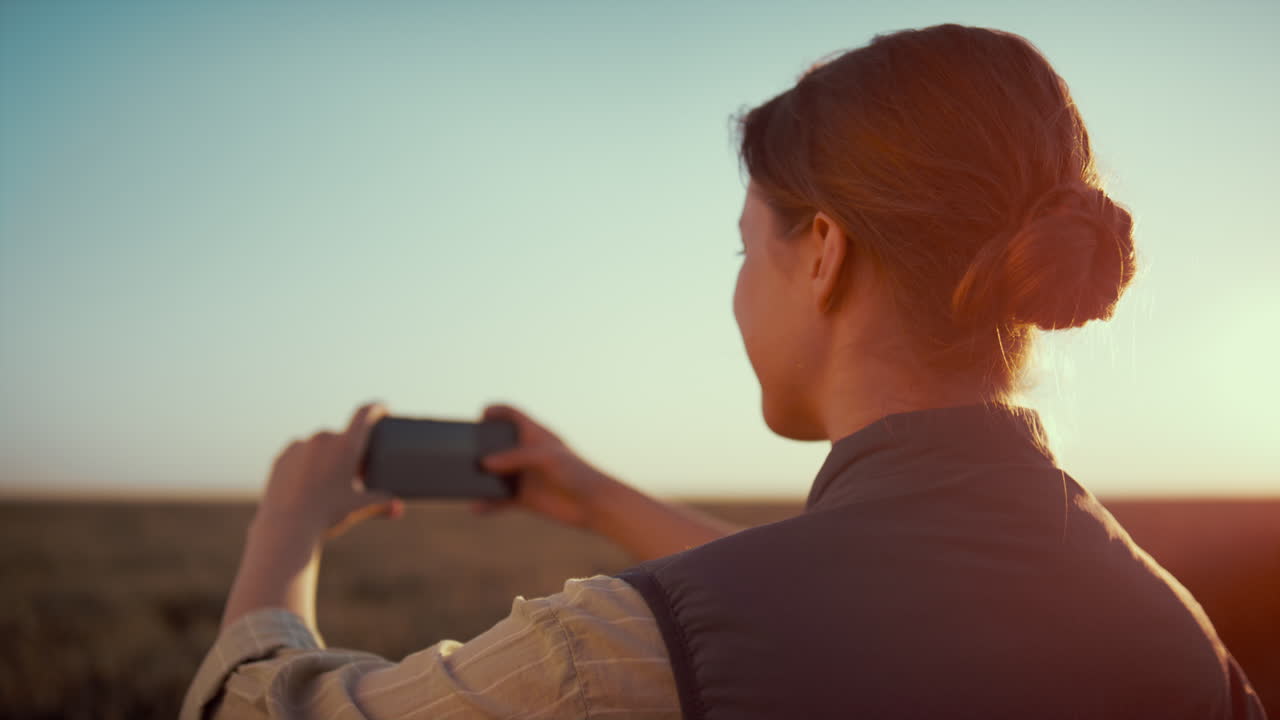 una mujer tomando una foto de un campo de trigo a la luz del sol dorado. la temporada agrícola de otoño.