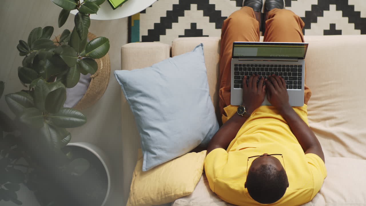 Afro-American Man Sitting on Sofa and Typing on Laptop