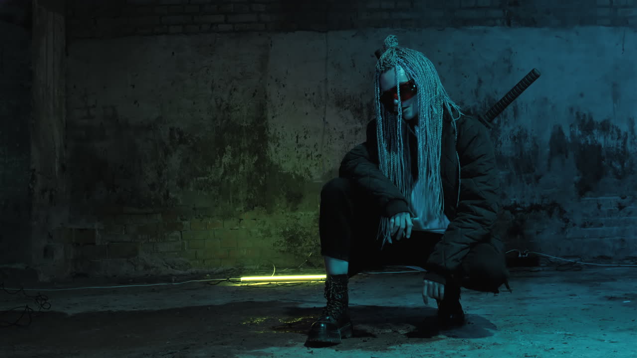 una chica con dreadlocks y katanas en cuclillas en gafas rojas y posa contra una pared de ladrillo de neón
