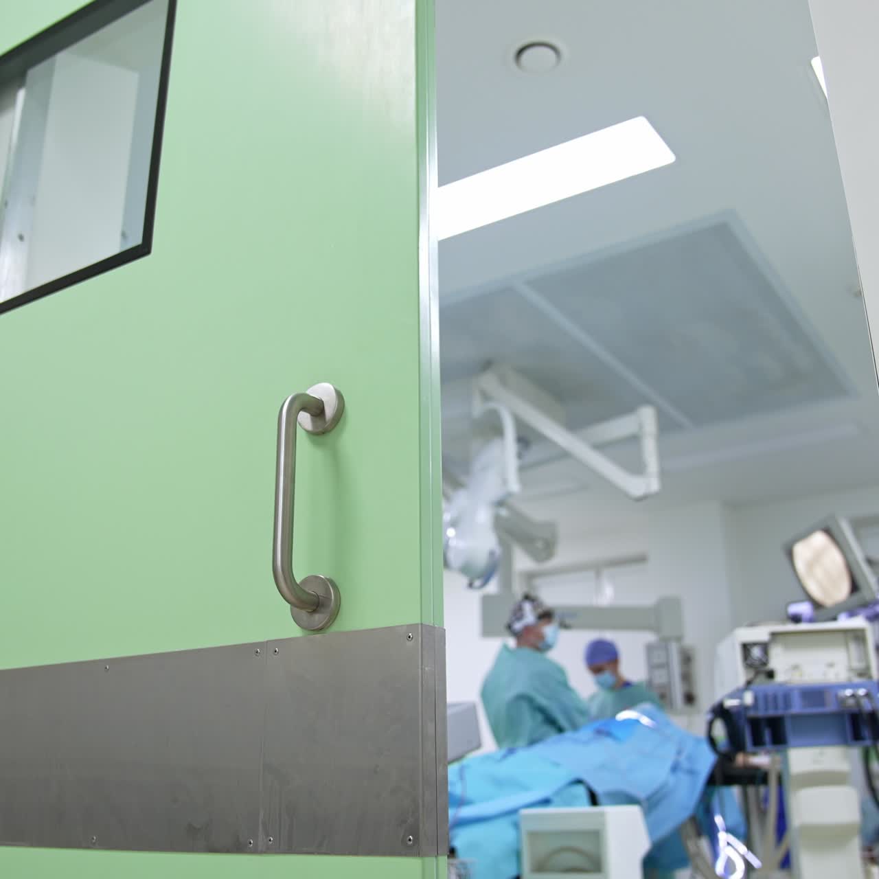 Portas abertas para um centro cirúrgico moderno com uma operação em andamento. Espiando o trabalho de profissionais médicos em um ângulo de visão baixo. Plano de fundo desfocado