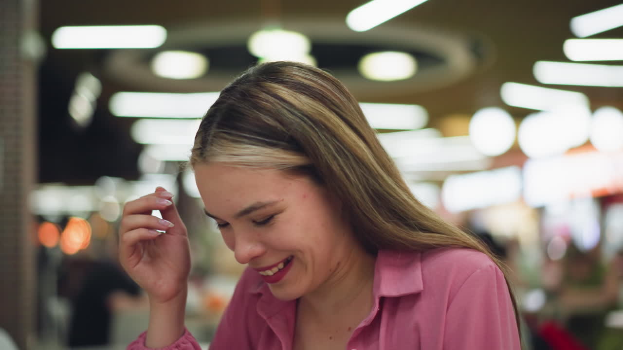 레스토랑에 앉아있는 분홍색 드레스를 입은 하 여자가 장난스럽게 그녀의 상단 입술에 감자 을 놓고, 그것이 수염인 척하고, 그것이 떨어지면서 그녀는 주변 사람들의 흐릿한 시야로 웃기 시작합니다.