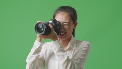 스튜디오에서 녹색 스크린 배경에 서서 사진을 찍는 카메라를 사용하는 아시아 사진작가의 클로즈업