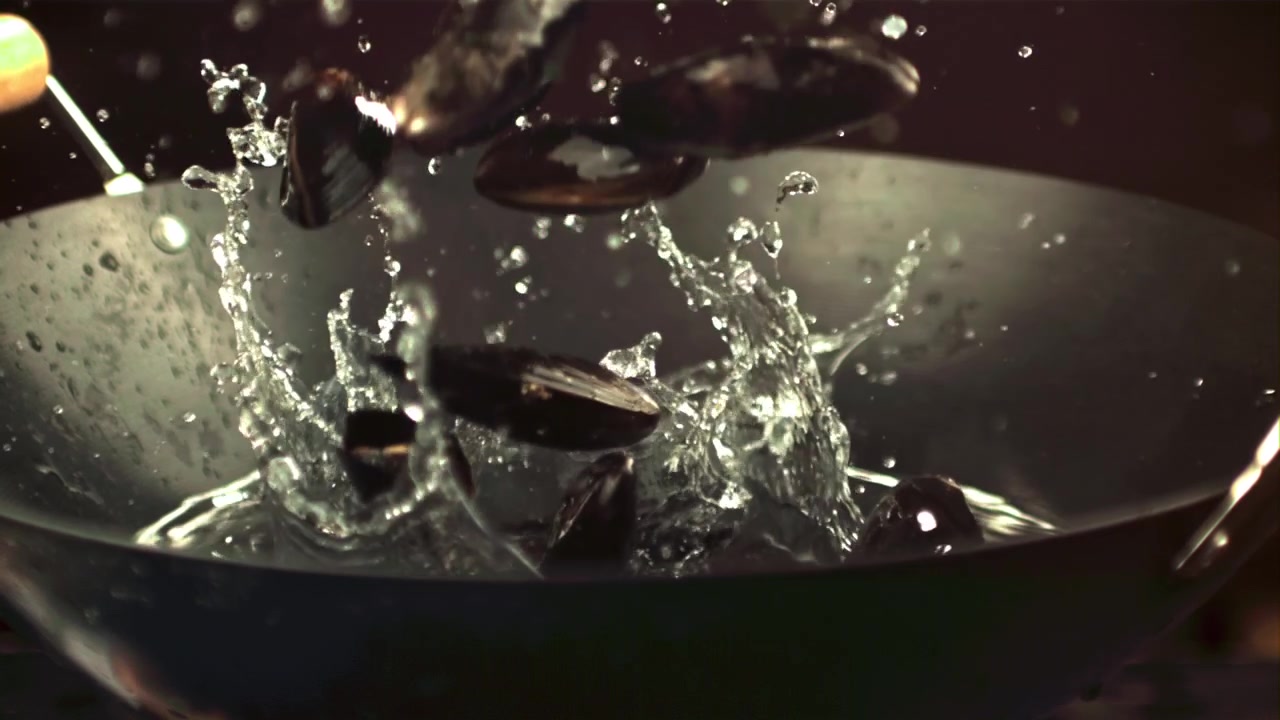 Cozze fresche che schizzano nell'acqua in un wok scuro.