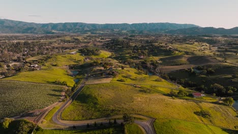 Drone-Volando-Lentamente-Sobre-Suaves-Colinas-En-La-Región-Vinícola-De-Santa-Ynez-California,-Viñedos-Debajo-Y-Cordillera-En-El-Horizonte