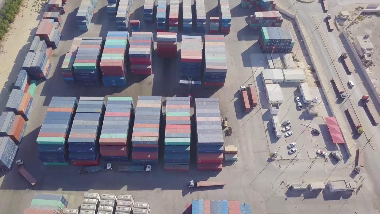 A fleet of trucks enter the massive container yard with colorful containers and loaders getting ready to be loaded with cargo