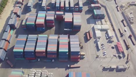 a fleet of trucks enter the massive container yard with colorful containers and loaders getting ready to be loaded with cargo