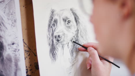 close up of artist sitting at easel drawing picture of dog in charcoal