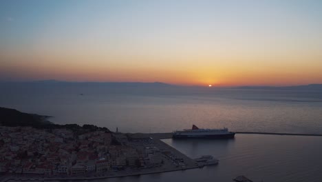 Aerial-drone-Flight-over-downtown-mitilini-revealing-sunrise-at-sea-with-ferry-to-athens,-lesvos,-greece