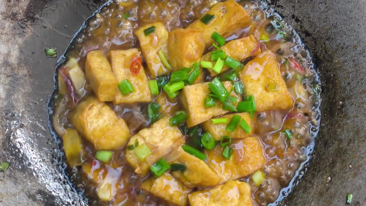 Tahu goreng pedas mendidih perlahan di wajan dengan saus gurih yang kaya. Masakan jajanan Asia lezat dengan uap mengepul. Ideal untuk konten kuliner dan memasak