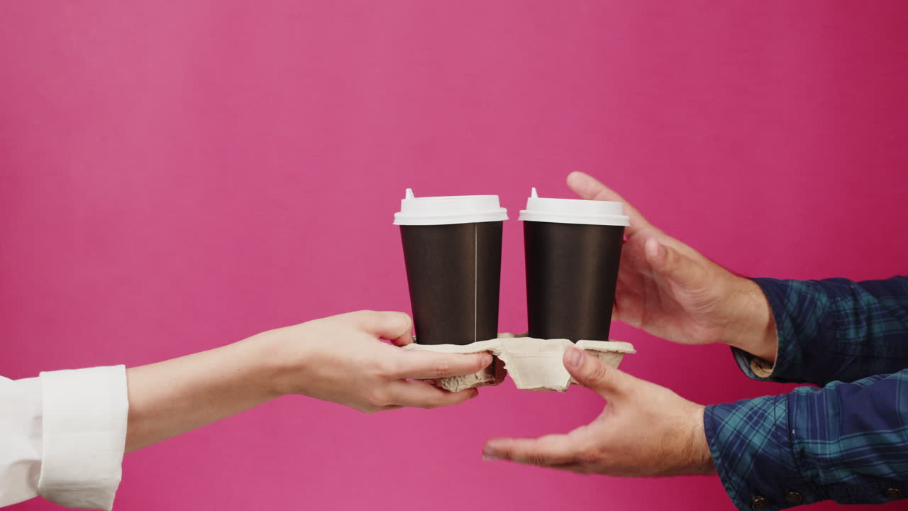Mani che si scambiano due tazze di caffè da asporto su sfondo rosa