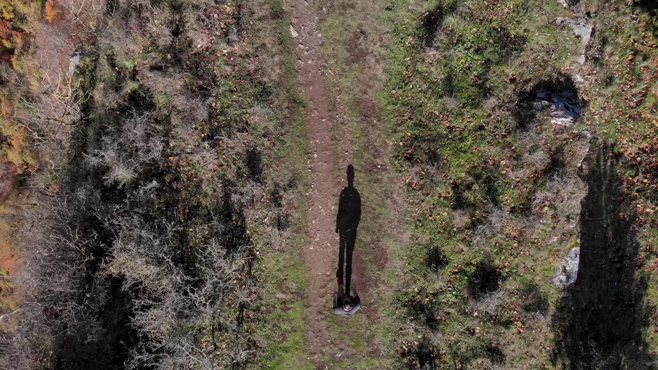 Aerial: zenital shot of a man and its shadow walking along a narrow plateau and close to the cliff
