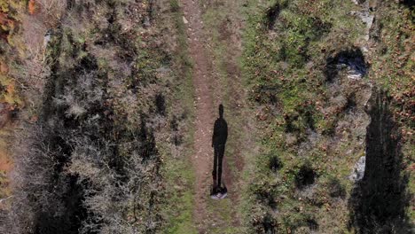aerial: zenital shot of a man and its shadow walking along a narrow plateau and close to the cliff