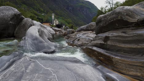 pan up along flowing waters smoothing rocks and stones to chapel in lavertezzo switzerland