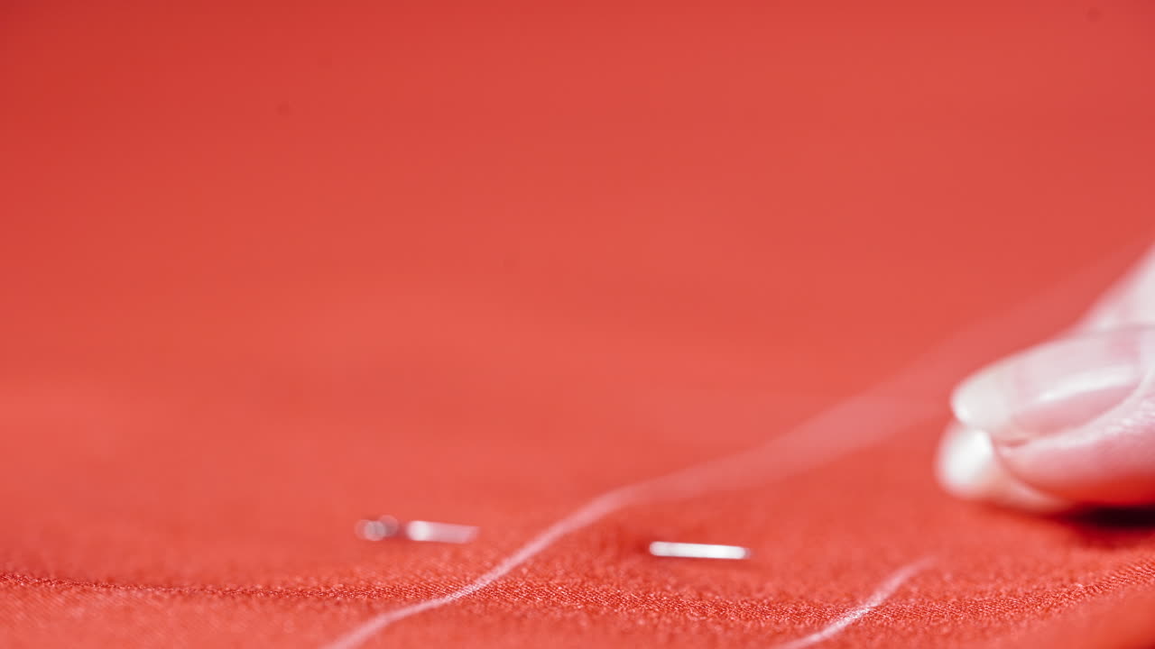Tailor's fingers are putting the pin to the red fabric. Red cloth with white lines and a dressmaker working with pins. Close-up. Concept sewing and handicraft.