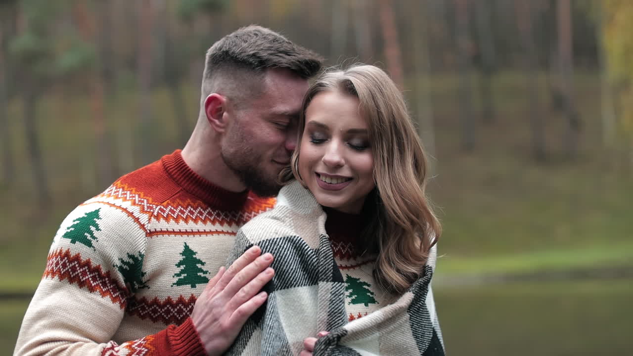 Man hugging his girlfriend in plaid standing behind her. Romantic date in the countryside near the river. Lovely couple at the backdrop of autumn nature.