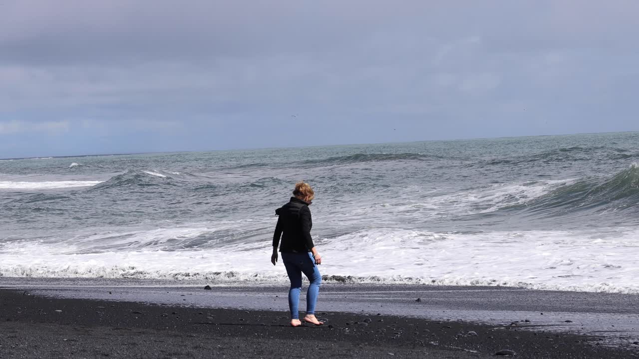 검은 해변에서 바위를 줍는 여자