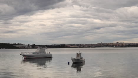 two boats moored on calm river in seixal, portugal on a cloudy day - wide shot