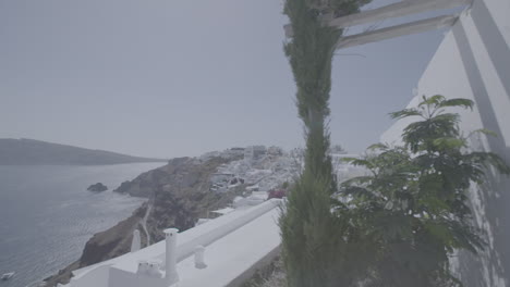 Overview-of-Santorini-Greece-on-a-sunny-day-seen-from-a-terrace-with-plants-in-front-in-slowmotion-and-the-sea-in-the-background-reflecting-the-sun-LOG