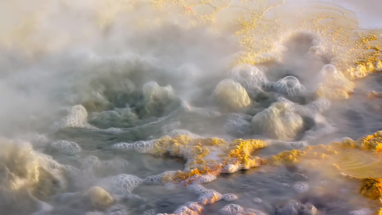 Sorgente termale geotermica ribollente con vapore, tappeti microbici giallo-arancio vivaci che rivestono una pozza acida bollente