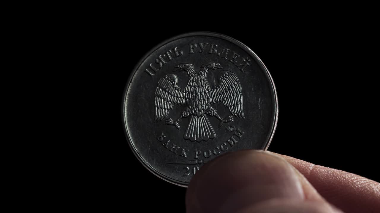 los dedos sostienen una moneda de 5 rublos rusos y la vuelven. concepto de depreciación, incumplimiento financiero o bancarrota. sanciones. intercambio de divisas. negocios con dinero. cabezas macro en fondo negro