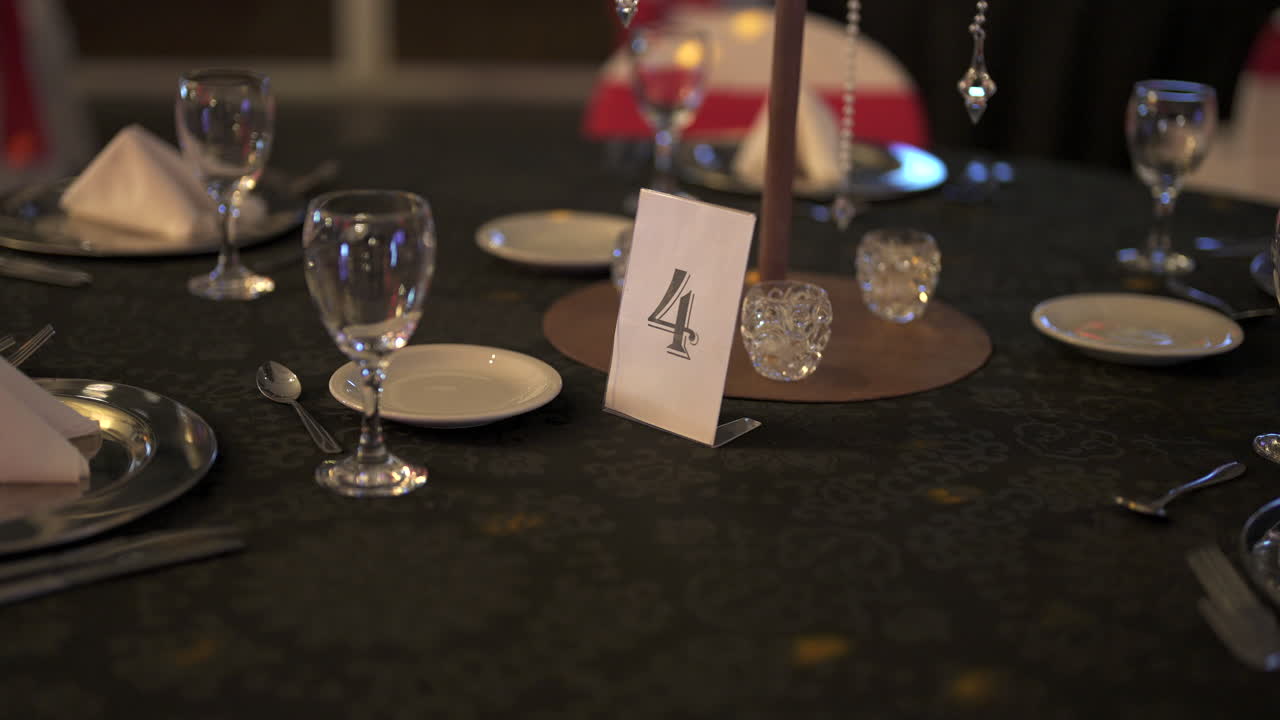 arreglo elegante de vasos, platos y pieza central en la mesa número cuatro, creando anticipación para los invitados en una recepción de boda de lujo, disparo en cámara lenta