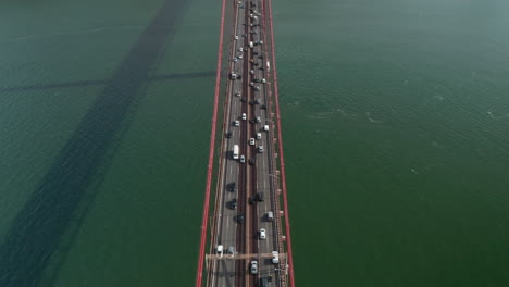 Vista-Aérea-Desde-Arriba-Después-De-Un-Intenso-Tráfico-Conduciendo-A-Través-Del-Mar-En-Un-Gran-Puente-Colgante-Rojo-Ponte-25-De-Abril-En-Lisboa,-Portugal