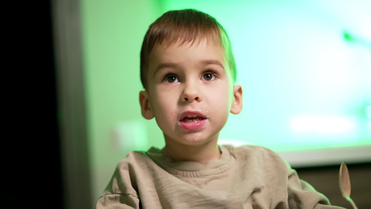 Calm baby boy with smudged face. Child eating dairy with a spoon. Close up. Blurred backdrop.