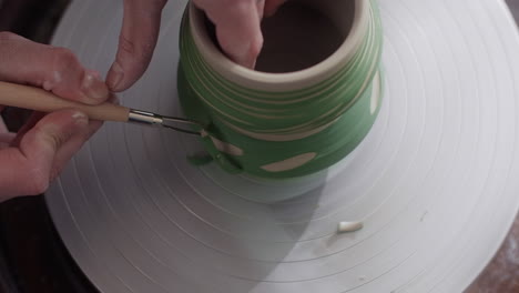 woman hand-painting a ceramic vessel on a pottery wheel