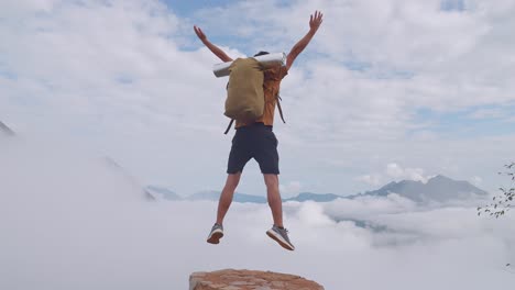 asian hiker male standing on the rock jumping happy and raising his hands celebrating reaching up top of foggy mountain