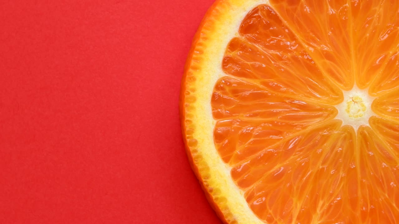una rebanada de naranja girando de cerca sobre un fondo rojo