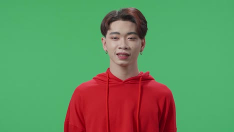 young asian transgender male smiling and emotionally flipping something while standing in the green screen studio