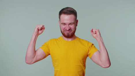 Stylish-man-in-t-shirt-shouting,-raising-fists-in-gesture-I-did-it,-celebrating-success,-winning