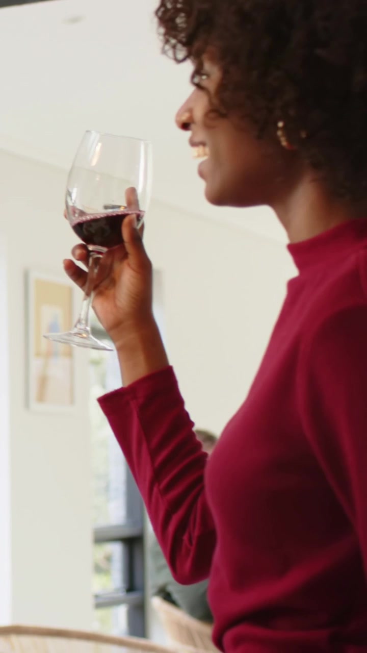 Vertical video: Holding wine glass, woman at home in maroon seeing guest toasting, copy space