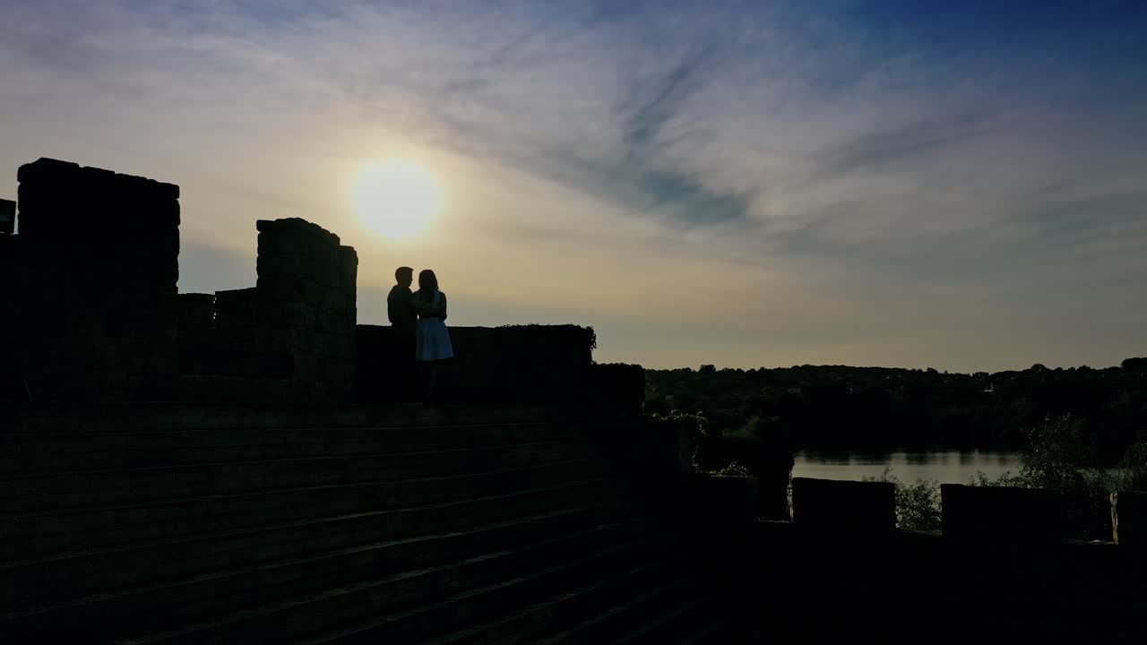 Lovely girl and her boyfriend meeting in an old castle near the river at dusk. Young beautiful couple standing together in the evening near lake.