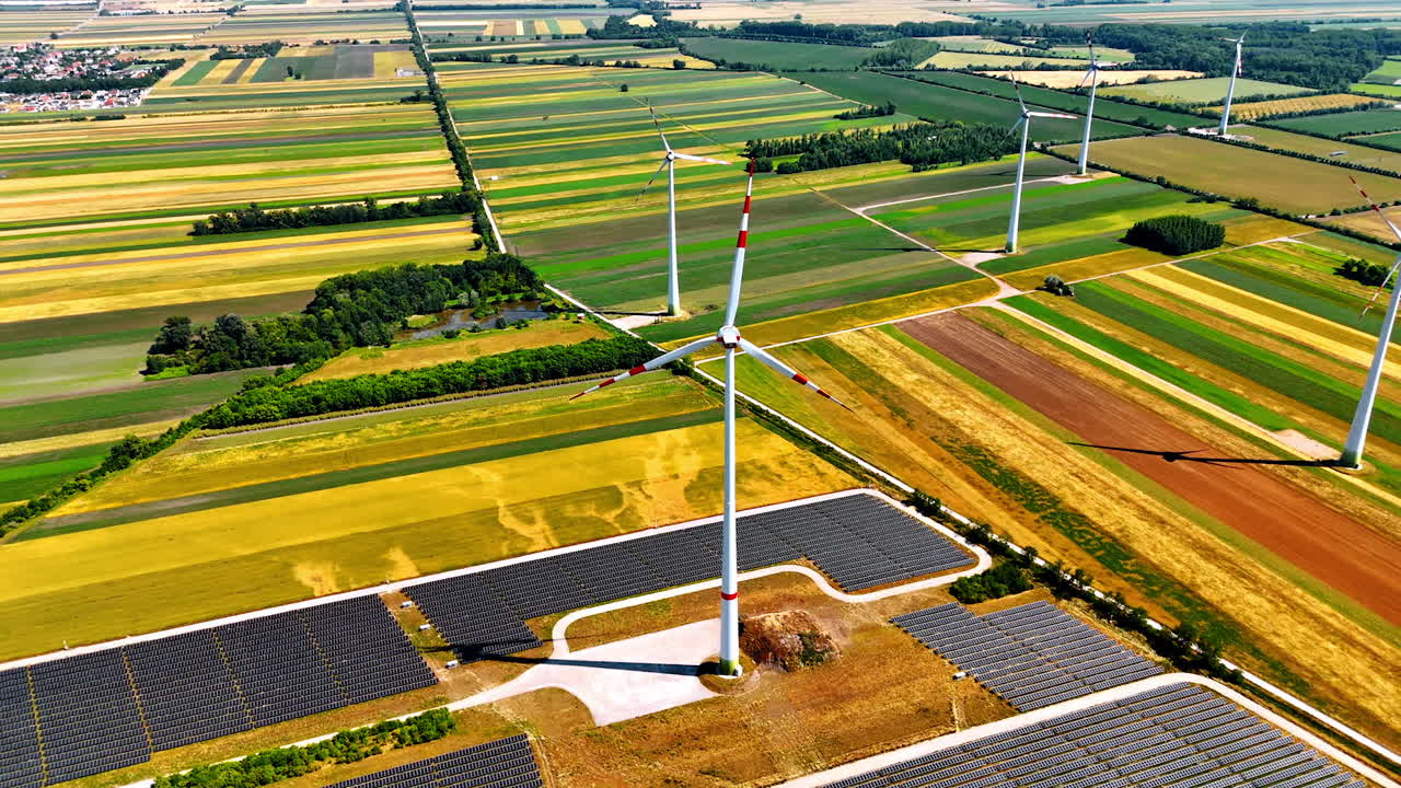 One of the windmills in the wind farm surrounded by the field of solar panels. Rising over the beautiful colorful plantations in the countryside used for green energy production