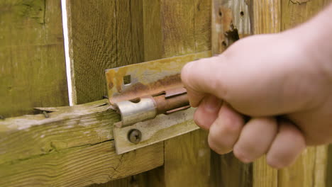 man unlatching old sliding lock and opening gate