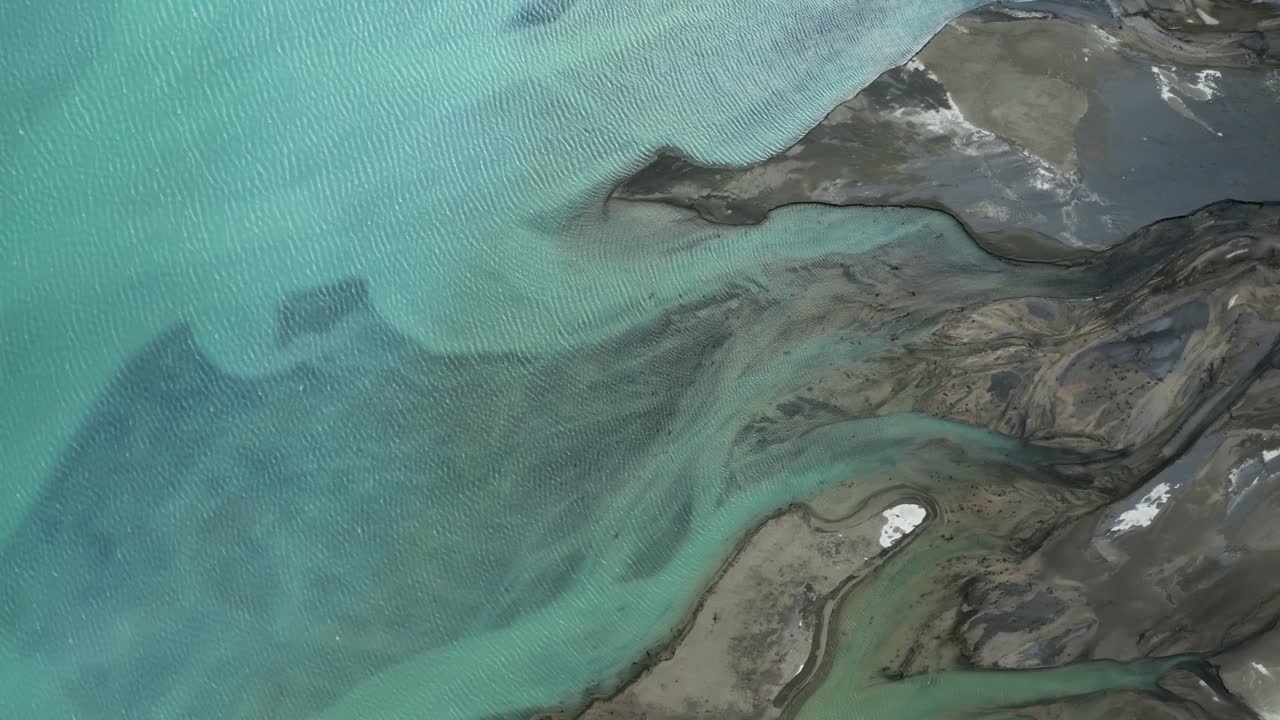 Top down aerial shot of mesmerizing glacial blue braided Tasman river flowing into turquoise Lake Pukaki, New Zealand