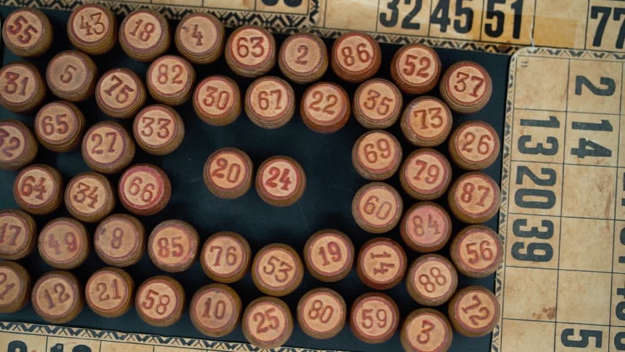 primer plano cinematográfico suave disparo desde arriba de una pila de barriles de madera de bingo en un cuadrado, figuras de madera, viejos números de fondo, juego de mesa vintage, cámara lenta 120 fps video comercial pan derecha