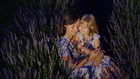 Mother-and-girl-daughter-kid-kissing,-laughing-in-aromatic-flowers-lavender-field-garden-at-night